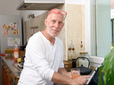 a senior man in kitchen using digital tablet and drink fruit juice