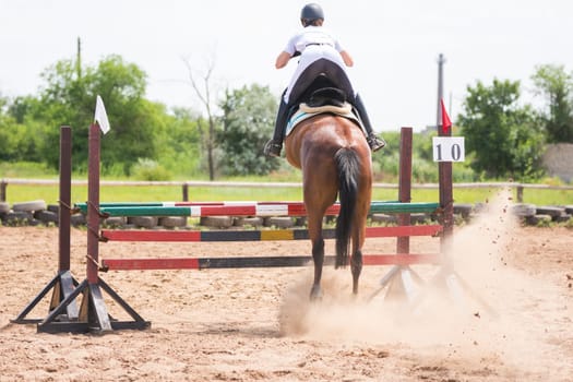Volgograd, Russia - June 19, 2016: Back view of a horse with a rider during take-off when jumping through a barrier