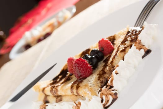 Fresh, golden pancakes with fruit and cream on a white plate with blurred background