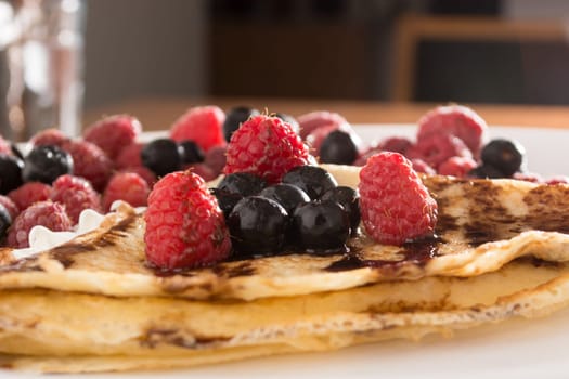 Fresh pancakes with fruit arranged all over it, and with cream