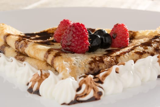 Fresh, golden pancakes with fruit and cream on a white plate with blurred background