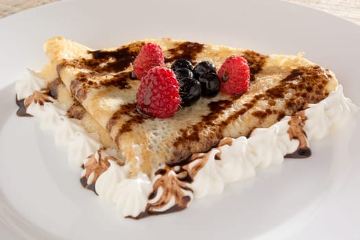 Fresh, golden pancakes with fruit and cream on a white plate with blurred background