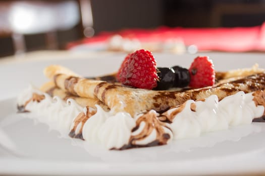 Fresh, golden pancakes with fruit and cream on a white plate with blurred background