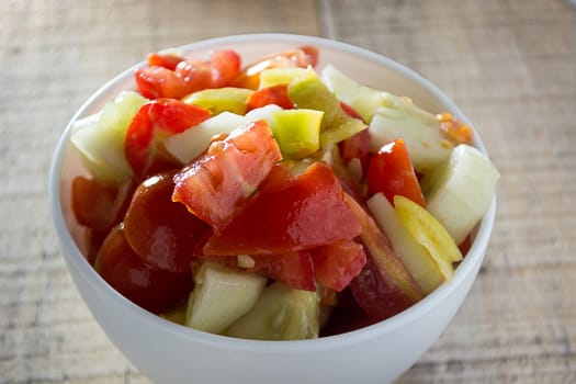 Cucumber and tomato sallad in the white dish on rustic wooden table
