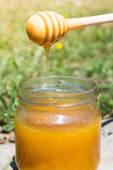 Jar full of sweet honey. Honey is dripping from a wooden honey stick
