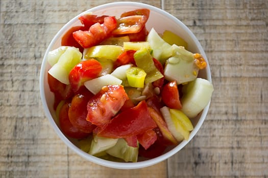 Cucumber and tomato sallad in the white dish on rustic wooden table