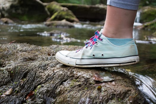 Girls foot stepping on a mossy rock. Blurry water stream in the background