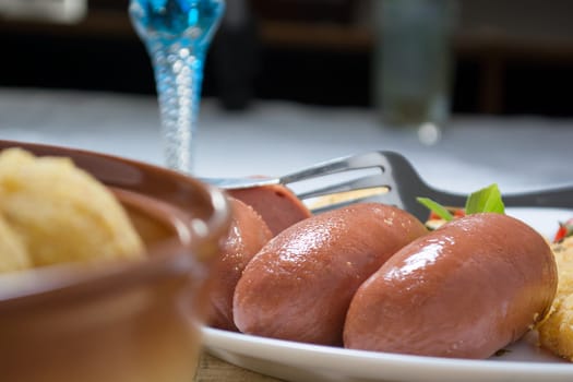 Pork sausages and breaded potatoes fried in a dish. Fork and knife next to dish