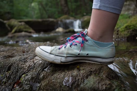 Girls foot stepping on a mossy rock. Blurry water stream in the background
