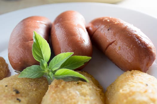 Pork sausages and breaded potatoes fried in a dish.