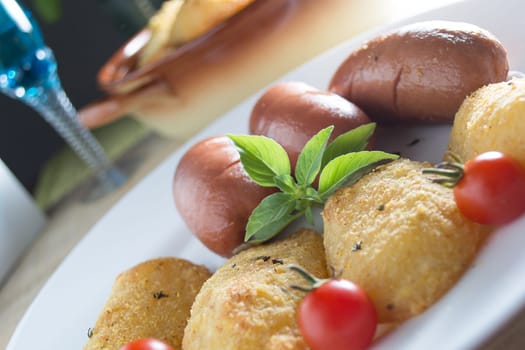 Pork sausages and breaded potatoes fried in a dish and decorated with cherry tomato