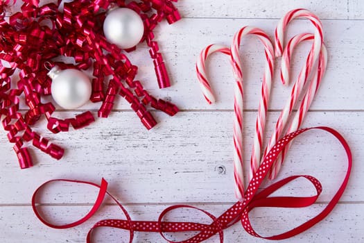 Christmas ribbons, ornaments and candy canes on white wooden table with copy space