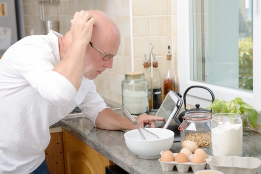 a senior man in kitchen using digital tablet