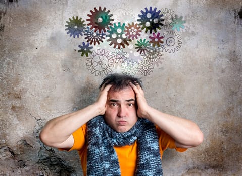 Bewildered looking man is releasing a thought train of cog wheels. Concerned facial expression. Both hands clasping head in a desperate gesture. Decaying background wall with textured surface.