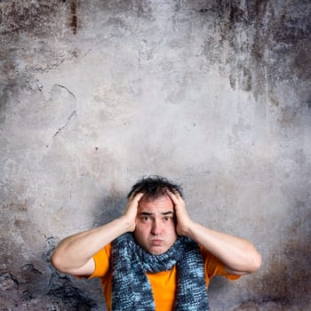 Adult man with a sulky facial expression clasping his head with both hands in an alarmed gesture. Pensive face with vacant frontal stare. Copy space across the empty center of a square composition.