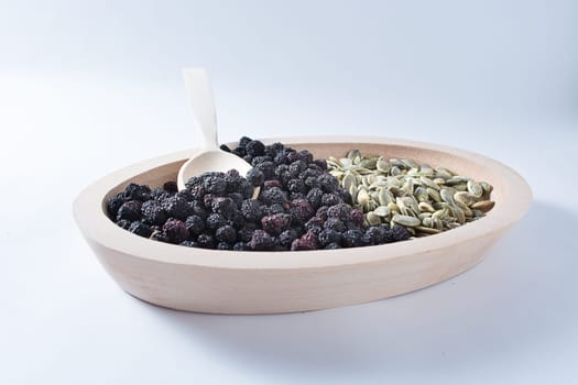 Aronia and pumpkin seeds in wooden bowl with wooden spoon isolated on white background