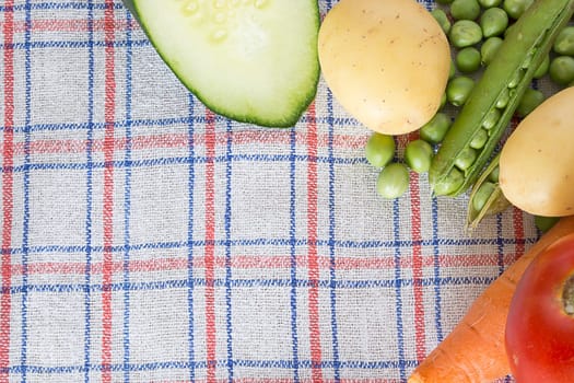 Various vegetable on a kitchen table in the corner of a shot. Carrots, potatoes, tomatoes, cucambers and green beans are visible