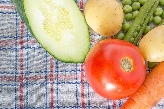 Various vegetable on a kitchen table in the corner of a shot. Carrots, potatoes, tomatoes, cucambers and green beans are visible