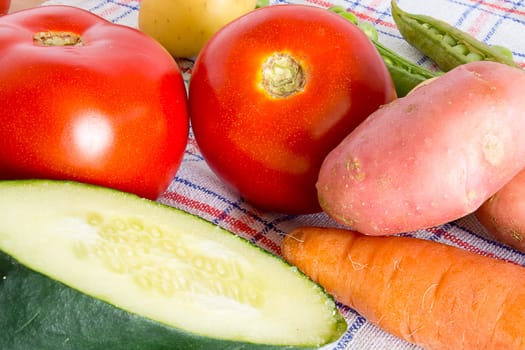 Various vegetable on a kitchen table. Carrots, potatoes, tomatoes, garlic, cucambers and green beans are visible