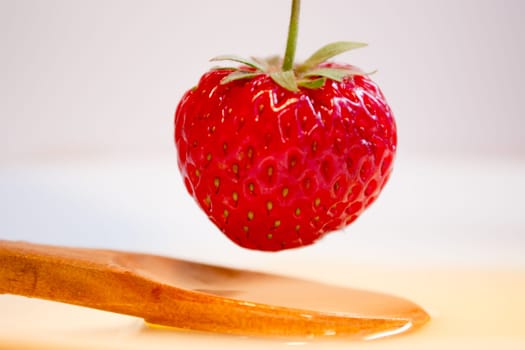 Strawberry hovering over wooden spoon and honey