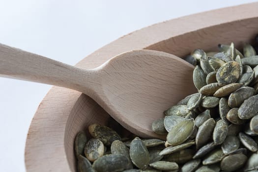 Pumpkin seeds in wooden bowl with wooden spoon isolated on white background