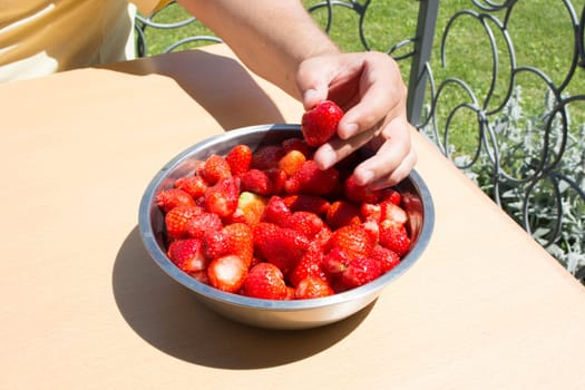Hand picking strawberries from metal bowl