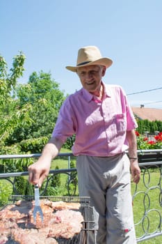 Senior man with fork in its hand grilling some food outside