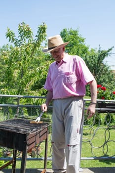 Senior man with fork in its hand grilling some food outside