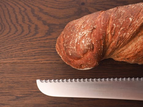 Delicious organic bread with a big bread knife on a wooden table with space for text