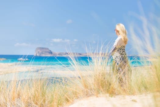 Relaxed woman wrapped in colorful scarf, enjoying sun, freedom and life at beautiful Balos beach in Greece. Concept of holidays, vacations, freedom, joy and well being.