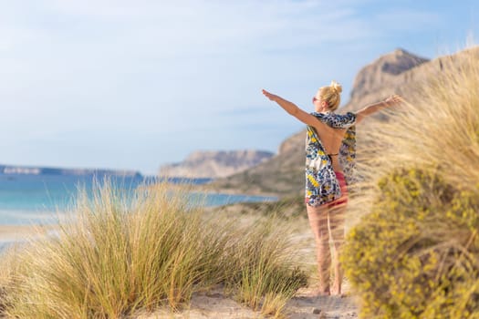 Relaxed woman wearing colorful scarf, enjoying sun, freedom and life at beautiful Balos beach in Greece. Concept of holidays, vacations, freedom, joy and well being.