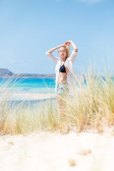 Relaxed woman wearing unpinned white shirt and black bikin, enjoying sun, freedom and life an a beautiful beach. Young lady feeling free, relaxed and happy. Concept of health well being.