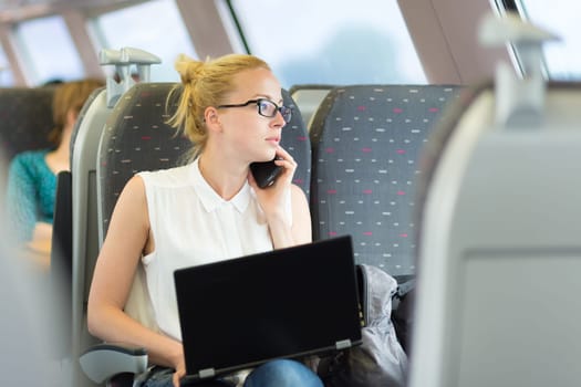 Businesswoman talking on cellphone and working on laptop while traveling by train. Business travel concept.