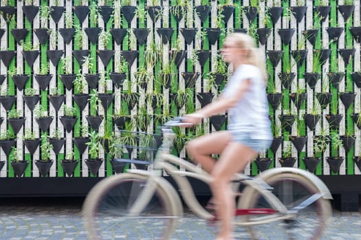 Motion blure of woman riding bycicle by green urban vertical garden wall in Ljubljana, European green capital of Europe 2016. Sustainable green city concept.