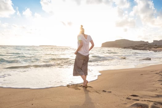 Woman walking on sand beach at golden hour. Seashore sunset walk.