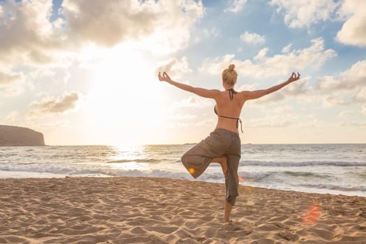 Active young woman practicing yoga on beach at sunset.