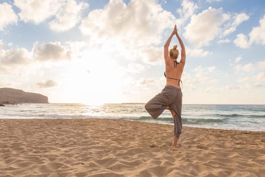 Active young woman practicing yoga on beach at sunset.