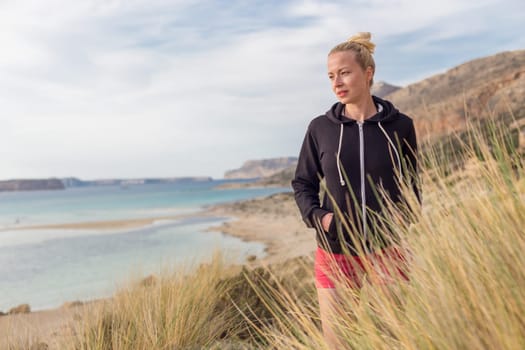 Relaxed woman in dark hoodie walking on serene Balos beach, Greece, enjoying beautiful nature and nice views.