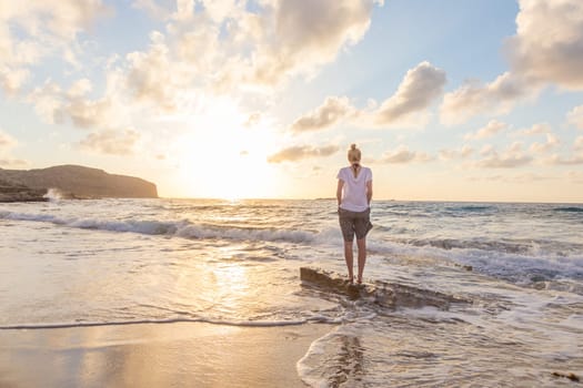 Relaxed woman enjoying sun, freedom and life an beautiful beach in sunset. Young lady feeling free, relaxed and happy. Concept of vacations, freedom, happiness, enjoyment and well being.