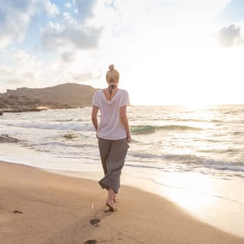 Woman walking on sand beach at golden hour. Seashore sunset walk.