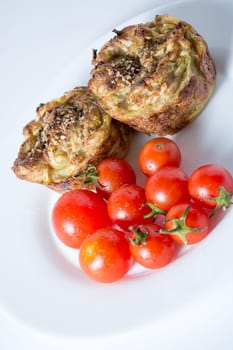 Ripe and red cherry tomatoes with zucchini muffins in white plate isolated on white background