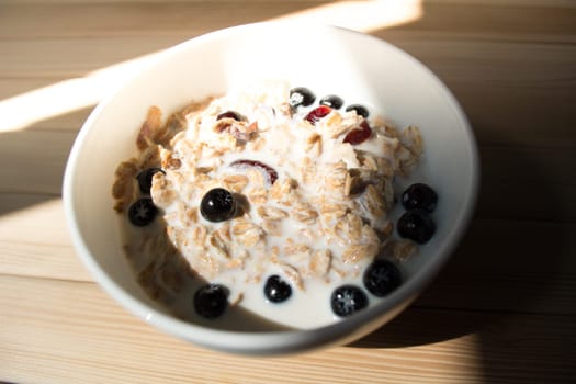 White bowl with healthy breakfast. Aronia and other berries with spelta  in milk