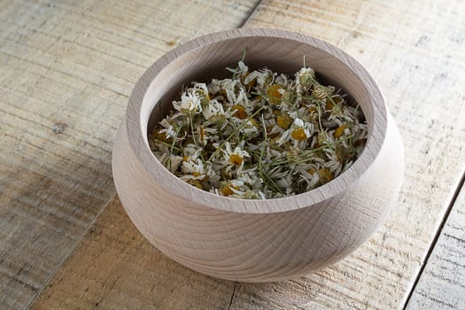 Dried chamomile flowers in wooden bowl placed on rustic table