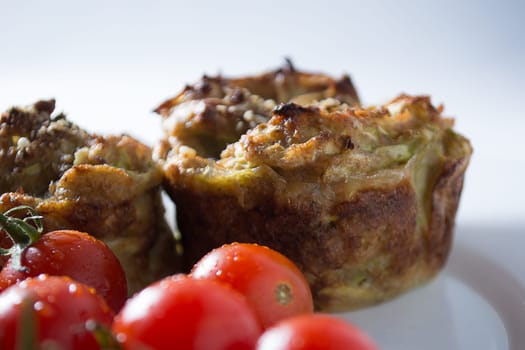 Ripe and red cherry tomatoes with zucchini muffins in white plate isolated on white background