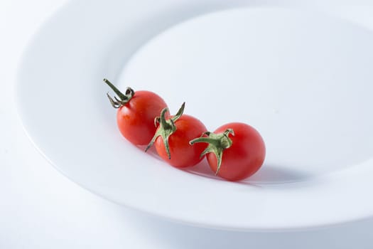 Ripe and red cherry tomatoes in white plate isolated on white background