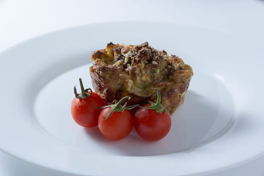 Ripe and red cherry tomatoes with zucchini muffins in white plate isolated on white background