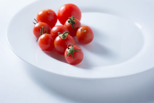 Ripe and red cherry tomatoes in white plate isolated on white background