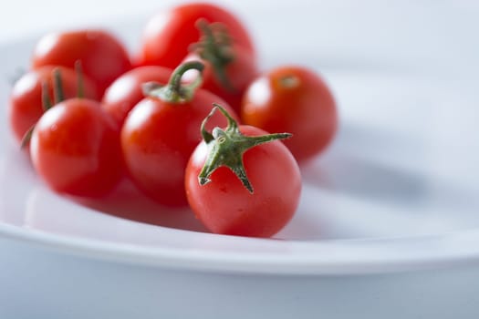 Ripe and red cherry tomatoes in white plate isolated on white background