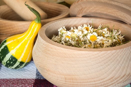 Dried chamomile flowers in wooden bowl placed on rustic table with decorative pumpkin
