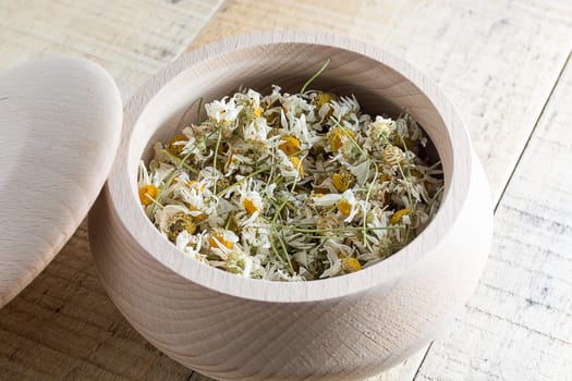 Dried chamomile flowers in wooden bowl placed on rustic table